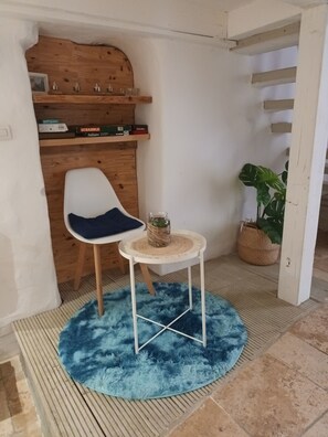 A small room with a white chair, a round table with a woven centerpiece, and a blue furry rug. - Charming studio, timeless atmosphere, pets welcome (Malaucène)