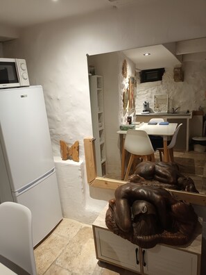 Eine kompakte Küche mit einem weißen Kühlschrank, einer Mikrowelle, einem Esstisch mit Stühlen und einer Dekoration auf einem Schrank.