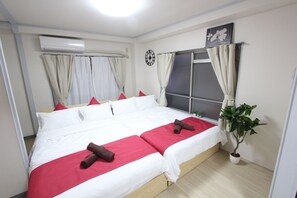 Un lit double avec une literie rouge et blanche, une plante en pot et une horloge au mur.