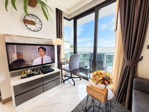Een moderne woonkamer met een televisie, een bank, een stoel, een bijzettafeltje met een bloevas en een balkon met uitzicht.