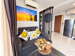 Un salon moderne avec un canapé, des coussins décoratifs, un arrangement floral et un tableau représentant un coucher de soleil.