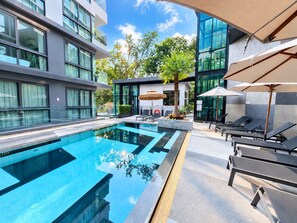 Een modern hotel met een zwembad, lounge fauteuils en een glazen gevel.