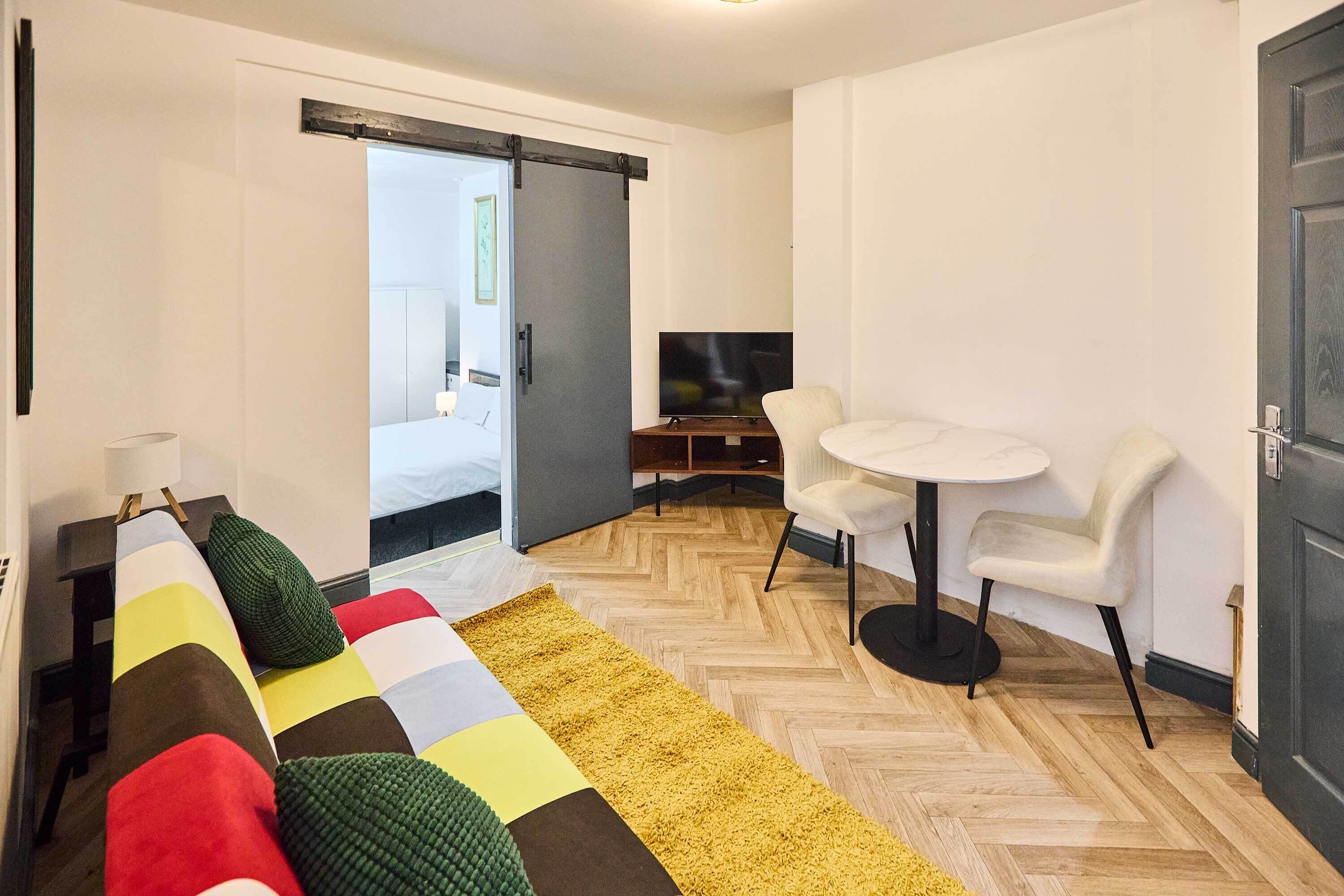 Una habitación de hotel moderna con sofá, una mesita redonda, televisor y una puerta corredera que da al baño.