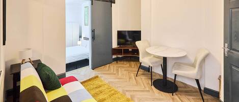 Una habitación de hotel moderna con sofá, una mesita redonda, televisor y una puerta corredera que da al baño.