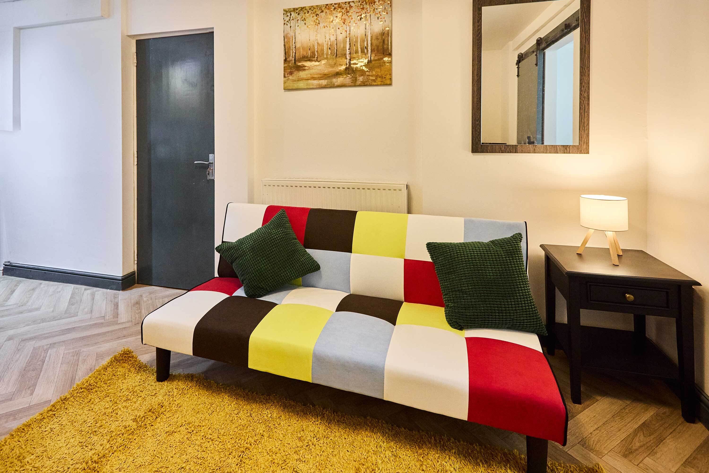 Une pièce avec un canapé, une petite table avec une lampe, une porte et un tableau au mur.