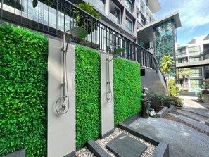 Um edifício moderno com um jardim vertical, guarda-corpo de metal e área de piscina com plantas e uma estátua.