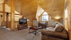 A cozy log cabin interior with a wooden ceiling, a television, a dining table with chairs, and a sofa.
