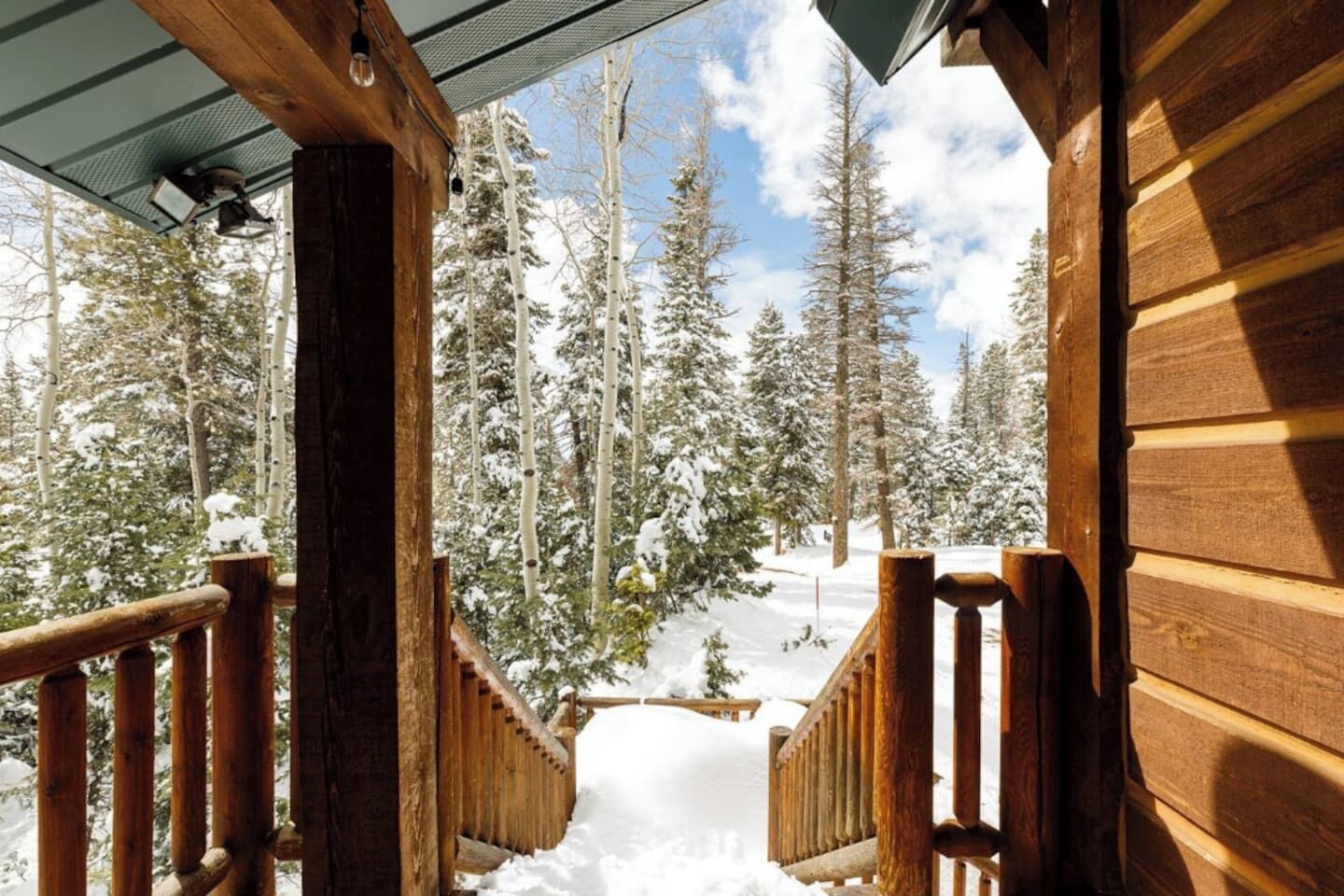 Une cabane en bois avec une terrasse enneigée et une vue sur une forêt couverte de neige.