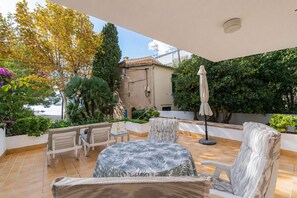 An outdoor patio with a table and chairs, surrounded by greenery and a view of the sea.