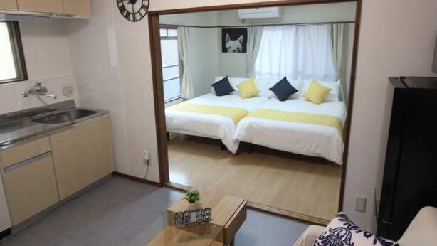 Een hotelkamer met een keukenhoek, een bed met twee kussens, een nachtkastje met een wekker en een spiegel die de kamer weerspiegelt.