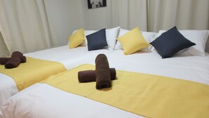 Twee bedden met witte lakens, gele en blauwe kussens en bruine handdoeken.