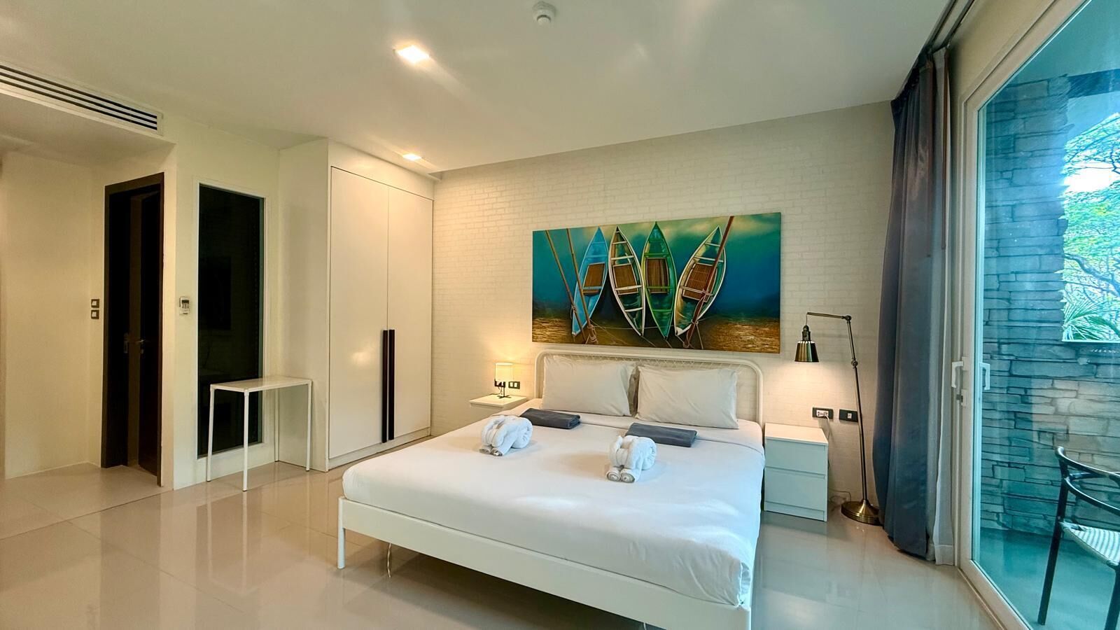 Een moderne hotelkamer met een groot bed, een schilderij van boten, een nachtkastje en uitzicht op het groen.
