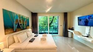 Ein Hotelzimmer mit einem großen Bett, einem Gemälde von Booten, einem Fernseher und einem Balkon mit Blick auf Bäume.