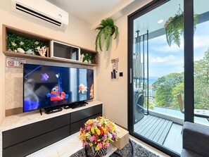 A modern living room with a flat-screen TV, a flower vase, and a balcony with a view. - A203 - 1 Bedroom Serviced Apartment with Seaview at Ao Nang Beach (Tambon Ao Nang)