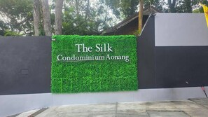 A sign for "The Silk Condominium Aonang" with a green hedge backdrop. - A203 - 1 Bedroom Serviced Apartment with Seaview at Ao Nang Beach (Tambon Ao Nang)