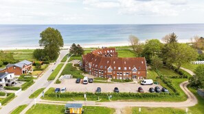 A large brick building with multiple windows and a parking lot in front. - Kiekut -2 balconies, playground, activity room, wellness area, sea view, parking (Kronsgaard)