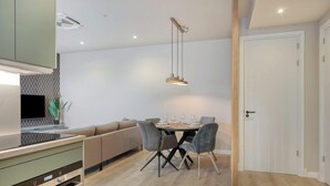 A modern kitchen with a built-in oven, a dining area with a wooden table and grey chairs, and a white door.