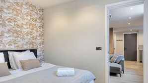 A modern bedroom with a large bed, a decorative wall, and a view into another room.