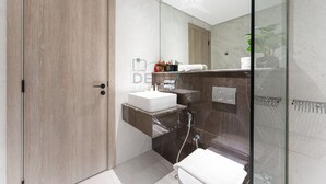 Een moderne badkamer met een houten deur, een witte wastafel, een glazen douchecabine en een spiegel die de ruimte weerspiegelt.