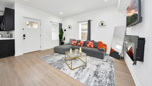 Ett modernt vardagsrum med en grå soffa, ett soffbord i glas och en väggmonterad TV.