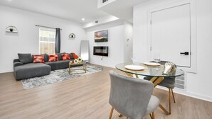 Ett modernt vardagsrum med en grå soffa, ett soffbord i glas och en matplats med ett vitt bord och stolar.