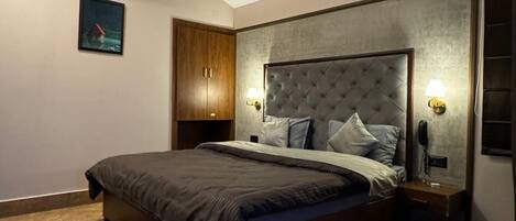 Une chambre avec un grand lit, une armoire en bois, un ventilateur de plafond, des lampes de chevet et une petite table.
