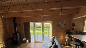 A cozy cabin interior with a sofa, a dining area, a kitchen, and a large window. - 3 Bedroom 2 Bath Chalet with hot tub in peaceful countryside close to Exeter (Broadclyst)