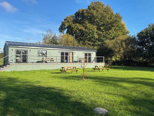 Een klein, lichtgroen gebouw met een plat dak, grote ramen en een overdekt terras met picknicktafels.