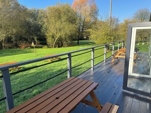 Een houten terras met picknicktafels en een hekwerk met uitzicht op een gazon met bomen.