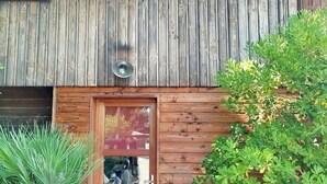 En träbyggnad med en trädörr och ett litet fönster. Framför dörren står krukväxter.