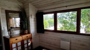 Ett rum med träväggar, ett fönster med utsikt över grönskan, ett träskåp med lådor, en hängande växt och en takfläkt.