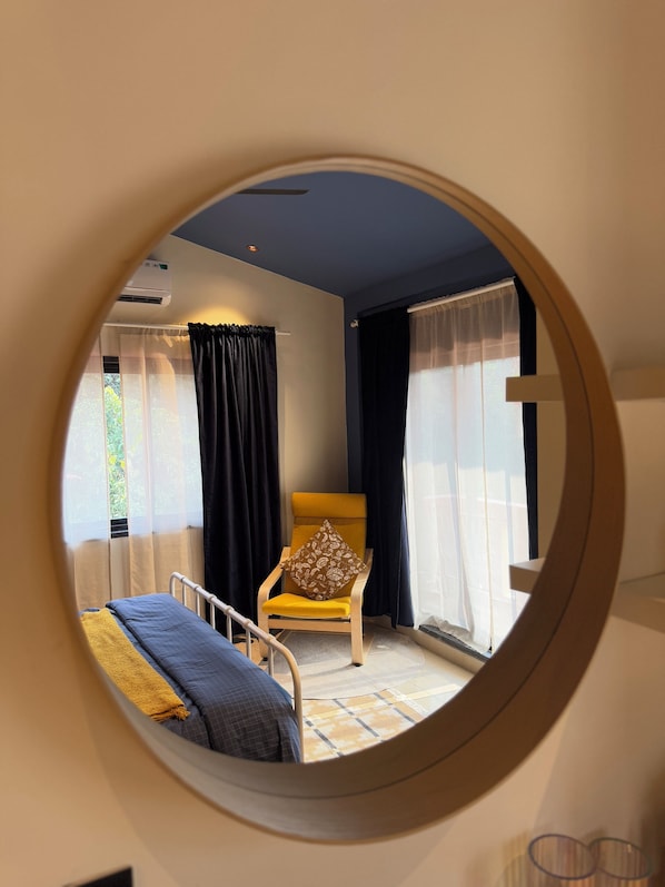 A room with a bed, a chair, and a round mirror on the wall.