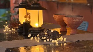 A cozy indoor setting with a star-shaped light fixture, two lanterns, and two clay pots on a reflective surface.