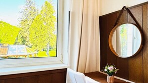 A room with a wooden ceiling, a window with a view of trees, a round mirror, a small table, and a chair. - Spacious Garden Villa for 16 Guests (Vienna)
