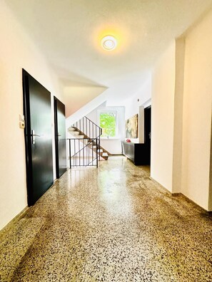 A hallway with a polished stone floor, a staircase with a metal railing, and a window with a view of greenery. - Spacious Garden Villa for 16 Guests (Vienna)