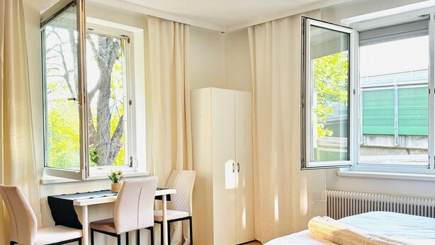 A bedroom with a bed, a desk, and a chair. There are windows with curtains, a radiator, and a wardrobe. - Spacious Garden Villa for 16 Guests (Vienna)