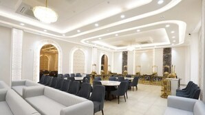 A spacious dining area with round tables and chairs, a bar area with gold accents, and a modern chandelier. - Su Casa Banquets and Hotel (Vikasnagar)