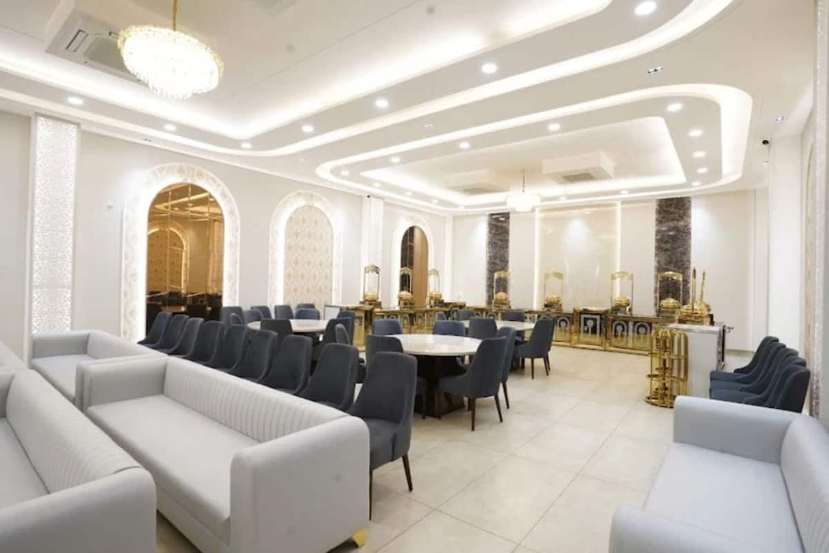 A spacious dining area with round tables and chairs, a bar area with gold accents, and a modern chandelier.