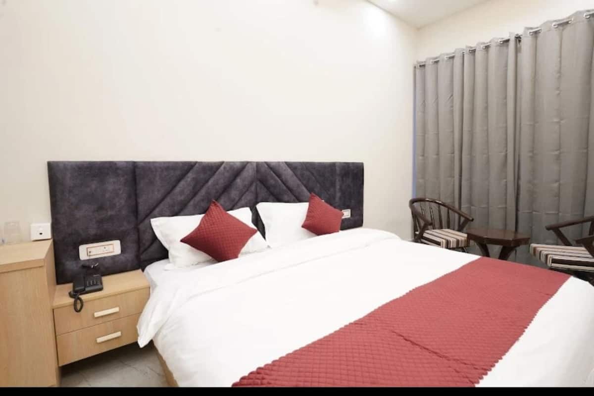 A hotel room with a bed, a nightstand, a chair, and a window with curtains.