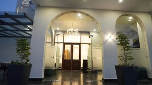 A building entrance with a glass door, arched windows, and potted plants. - Su Casa Banquets and Hotel (Vikasnagar)