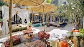 A cozy outdoor seating area with thatched umbrellas, plush seating, and a pool in the background. - Riad Mazarin des gourmets (Marrakech)