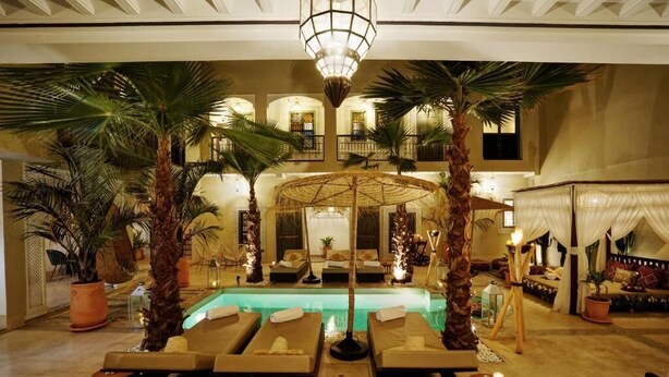 A luxurious indoor pool area with lounge chairs, palm trees, and a central water feature. - Riad Mazarin des gourmets (Marrakech)