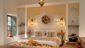 A well-appointed bedroom with a large bed, two wall-mounted lamps, a decorative wall piece, and a bedside table with a camera and books. - Riad Mazarin des gourmets (Marrakech)