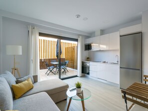 A modern apartment with a living room, a glass dining table, a sofa, a kitchen with white cabinets, a refrigerator, and a sliding glass door leading to a balcony. - Golden Coast By CanariasGetaway (Mogán)