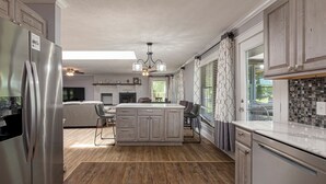 A modern kitchen with a central island, stainless steel appliances, and a dining area with a view. - Waterfront Retreat with Hot Tub (Marion)