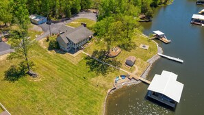 An aerial view of a lakeside property with a large house, dock, and boats. - Waterfront Retreat with Hot Tub (Marion)