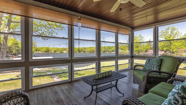 A covered patio with wicker furniture, large windows, and a table with a sign. - Waterfront Retreat with Hot Tub (Marion)
