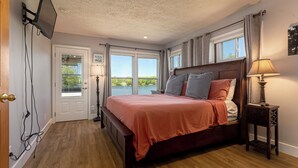 A bedroom with a bed, a nightstand, a TV mounted on the wall, and a window with a view of a lake. - Waterfront Retreat with Hot Tub (Marion)
