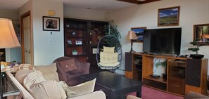 A living room with a sofa, a hanging chair, a television, a bookshelf, and a lamp. - 2-bedroom mountain getaway in Bretton Woods with A/C, family-pet friendly (Carroll)