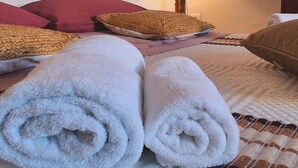 A neatly made bed with rolled white towels, a red headboard, and a lamp on a bedside table.
